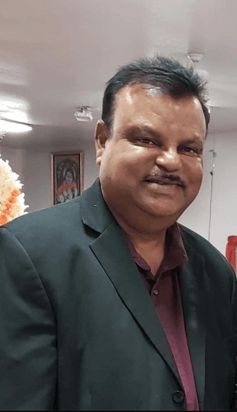 Middle-aged man with a mustache, smiling and wearing a dark blazer over a maroon shirt.